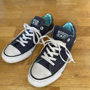Converse All Star mörkblå sneakers - Snygga Converse All Star sneakers i mörkblå canvas med vita gummisulor och vita snören. Insidan har ett unikt färgglatt mönster i grönt, blått och vitt. Klassisk låg modell med rund tå och platt sula. Lite smutsiga där framme men i bra skick, köpta second hand🫐💙