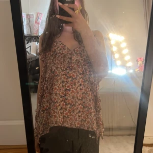 Blommig volangtop med tunna axelband - Supersöt blommig topp med volangdetaljer och tunna axelband. Toppen har en luftig passform och är perfekt för varma dagar. Färgerna går i rosa, vit, blå och beige med små blommor över hela tyget. Materialet känns lätt och flowy. Jag säljer dd för att den är förstor 💖