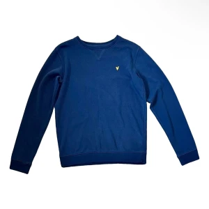 Lyle & Scott sweatshirt  - Snygg marinblå sweatshirt från Lyle & Scott med klassisk rund hals och gul broderad logga på bröstet. Tröjan har långa ärmar och ribbade muddar vid ärmslut och nederkant. Perfekt för dig som gillar stilren och enkel design.