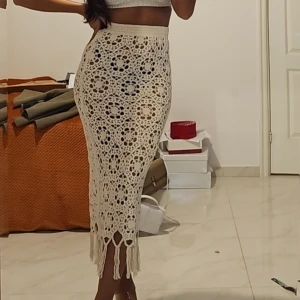 Beige virkad långkjol med fransar - Säljer en beige virkad långkjol med snyggt hålmönster och fransar längst ner. Kjolen har en hög midja och sitter tight över höfterna. Perfekt för dig som gillar boho-stil och vill sticka ut med coola detaljer.