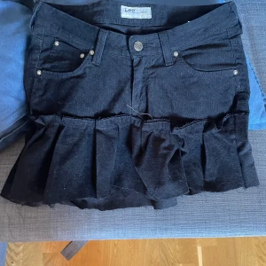 Svart manchesterkjol från Lee egensydd - Supersnygg svart kortkjol från Lee som jag har sytt själv i manchester med volangdetalj nedtill. Kjolen har klassiska jeansfickor fram och bak, bälteshällor och knäppning framtill. Perfekt för dig som vill ha en edgy och trendig look.
