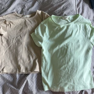 Två basic t-shirts från Gina Tricot - Säljer två stilrena t-shirts från Gina Tricot, båda i storlek S. Ena är ljusbeige och andra är ljusgrön, båda med rund hals och korta ärmar. Perfekt till jeans eller kjol, mjukt bomullsmaterial och klassisk passform. Båda t-skirtsen är lite tajtare passform