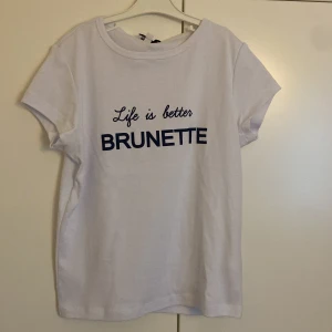 Vit t-shirt med tryck från Subdued - Vit t-shirt från Subdued med blått tryck på bröstet där det står 'Life is better BRUNETTE'. Modellen är klassisk med rund hals och korta ärmar. Perfekt för dig som gillar statement-plagg.