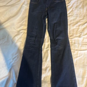 Levi's 725 Bootcut jeans blå - Snygga Levi's 725 High Rise Bootcut jeans i mörkblå denim. Modellen har hög midja och klassisk bootcut-passform som ger en schysst siluett. Jeansen har fem fickor, gul kontrastsöm och Levi's läderpatch bak. Perfekta för dig som gillar retrovibbar och tidlös stil.