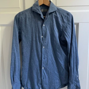 Canali skjorta  - Snygg blå skjorta från Canali i slim fit-modell. Skjortan har en cut-away krage, vita knappar och långa ärmar. Materialet är otroligt mjukt och stretchigt, perfekt för dig som gillar stilren och bekväm design. Passformen är smal och modern.