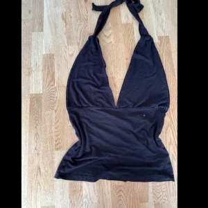 Svart halterneck topp med knyt - Svart halterneck topp med djup v-ringning och knyt i nacken. Toppens form är figurnära och den är ärmlös, perfekt för att skapa en cool och enkel look. Materialet känns mjukt och stretchigt, troligen bomull eller polyester. Snygg att styla med jeans eller kjol.
