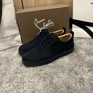 Mörkblå sneakers från Christian Louboutin - Snygga mörkblå sneakers från Christian Louboutin i mocka med klassisk röd sula och diskret broderad logga på hälen. Skorna har rund tå, platt sula och mörkblå snörning. Insidan är beige och ger en lyxig känsla. Perfekt för dig som gillar exklusiva detaljer.