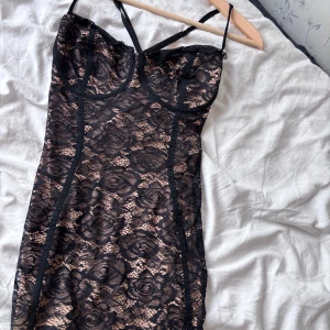 Svart spetsklänning från SHEIN - Supersnygg svart spetsklänning från SHEIN i storlek L. Klänningen har beige underton, blommigt spetsmönster och smala axelband som korsas i ryggen. Figurnära passform och kort längd, perfekt för dig som vill sticka ut med en elegant och trendig look. Aldrig använd 