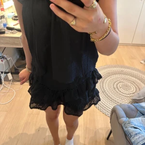 Svart volangkjol med resårmidja - Supersöt svart kortkjol med volanger och resår i midjan. Kjolen har en luftig känsla och är perfekt för dig som gillar en feminin och trendig stil. Materialet känns lätt och flowy, och volangdetaljerna ger extra rörelse.