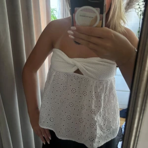 Vit bandeau tubtopp med broderi - Superfin vit bandeau tubtopp med twistad överdel och broderade blommor i tyget. Är i storlek S och är aldrig använd.