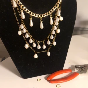 Andgjorta smycken likna den marianoslptter Skirv för frågor   - Första halvplan det kostar Unikt halsband 500 andra kostar 2000 och sista kostar 250   Och det sittas är sötvattenspärlor  i guldton med flera lager kedjor och hängande vita pärldroppar. Kedjorna har olika tjocklek och pärlorna är både runda och droppformade, vilket ger en cool och lyxig vibe. Perfekt för att lyfta din outfit med lite extra bling.