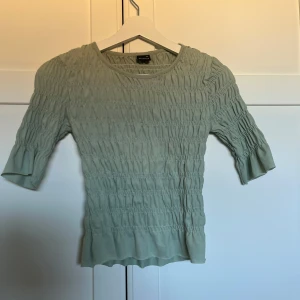 Ljusgrön ribbad topp från Gina Tricot - Supersöt ljusgrön topp från Gina Tricot i storlek XS. Toppen har ribbad struktur med smock över hela och trekvartsärmar med lätt volang vid ärmslutet. Perfekt för vår och sommar, och den mjuka bomullen gör den riktigt skön att ha på sig.