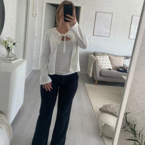 Vit kofta med knyt från 157 - Supersöt vit kofta från 157 med knyt framtill vid halsen. Modellen är öppen och har långa ärmar, perfekt att slänga över en topp. Storlek 160 men passar någon som bär xs.