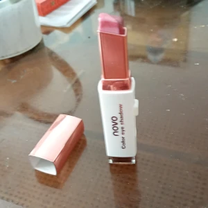 Novo rosa ögonskugga stick - Säljer en ögonskugga i stick-format från Novo. Färgen är en skimrande rosa med metallisk finish. Förpackningen är vit med roséguldigt lock och har en modern, fyrkantig design. Perfekt för att snabbt ge ögonlocken färg och glow.