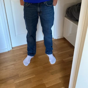 Nudie Jeans Gritty Jackson Blue Soil - Säljer ett par Nudie Jeans Gritty Jackson Blue Soil i klassisk mörkblå färg. Jeansen har rak passform och är tillverkade i 100% bomull. Snygga kontrastsömmar och fem fickor ger en clean och tidlös look. De är i bra skick då de är använda bara ett fåtal gånger. Nypris 1600kr.