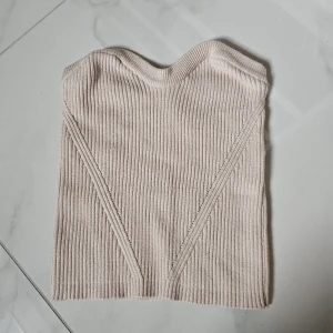 Beige ribbad bandeau tubtopp - Snygg beige bandeau tubtopp med ribbad struktur och subtila sömdetaljer framtill. Toppen är axelbandslös och har en mjuk, stretchig passform som sitter tight mot kroppen. Perfekt för att styla med jeans eller kjol för en trendig look.