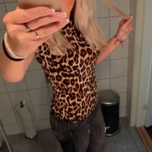 Leopardmönstrad ärmlös topp - Säljer en snygg ärmlös topp med leopardmönster i bruna och svarta toner. Modellen är tight och har rund hals, perfekt för dig som vill sticka ut med ett djuriskt print. Passar dig som gillar att ha en edgy och trendig stil. Osäker på storlek 