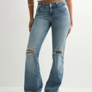 Bootcut jeans med slitningar från Nelly - Snygga ljusblå bootcut jeans från Nelly med slitna detaljer vid knäna och coola broderade fickor bak. Jeansen har klassisk femficksdesign, knapp och dragkedja framtill samt en skön passform med lite utsvängda ben. Använda runt 3-4 gånger. 