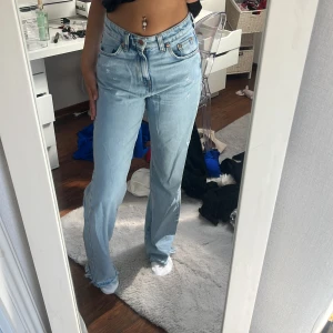 ljusblå jeans med fransad kant - Säljer ett par ljusblå jeans med hög midja och raka ben. Jeansen har klassiska fem fickor, knappgylf och fransad kant längst ner för en chill vibe. Tillverkade i jeansmaterial och har en relaxed passform som är både snygg och bekväm. 