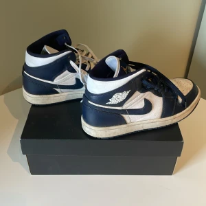 Nike Air Jordan 1 Mid vit/mörkblå - Nike Air Jordan 1 Mid i marinblått och vitt med klassisk Jordan-logga på sidan av skon. Box medföljer! Bra skick, lite smutsiga men tvättar såklart rent innan jag skickar! Nypris ligger runt 1300 , mitt pris på 399. Modellen heter White / Metallic Gold Obsidian. 