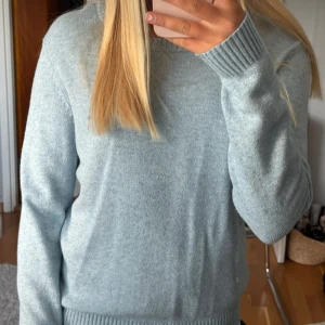 Ljusblå stickad tröja med rund hals - Mysig ljusblå stickad tröja med rund hals och ribbade muddar vid ärmslut och nederkant. Perfekt för dig som gillar enkel och clean stil. Tröjan har lång ärm och är i ett mjukt material som känns skönt mot huden.