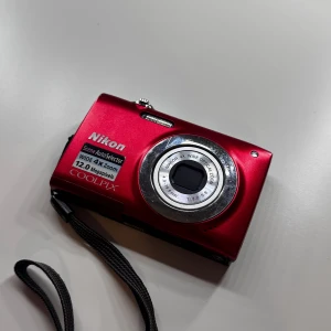 Digital kamera- Nikon Coolpix – 12 MP, 4x Zoom – Röd - 📸 Nikon Coolpix – 12 MP, 4x Zoom – Röd 📸  Säljer min fina Nikon Coolpix digitalkamera i mycket gott skick.Perfekt liten kamera för dig som vill ha något smidigt men ändå med bra bildkvalitet!  ✅ Batteri ingår ❌ Minneskort ingår ej  Skick & funktion: 	•	Kameran är välvårdad och fungerar som den ska. 	•	Ibland kan skärmen visa lite ljusreflektioner när man riktar kameran mot starka ljuskällor (ex. lampor eller solen), men det påverkar inte bilderna – de blir fina när de väl är tagna. 	kostade 5000