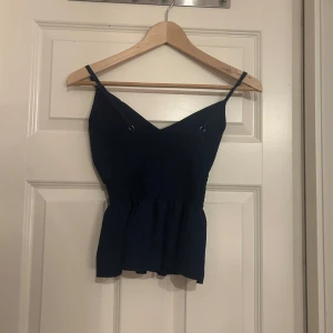 Mörkblå linnetopp med smock - Supersnygg mörkblå linnetopp med smala axelband och v-ringad hals. Toppen har smockad midja som ger en schysst passform och en lätt volang nedtill. Perfekt att styla med jeans eller kjol för en chill look.