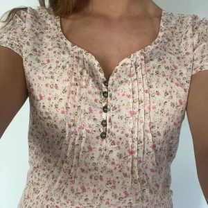 Blommig ljusrosa topp!!💞🫰🏻 - Supersöt somrig  blus i ljusrosa med små blommor!! Toppen har korta ärmar, v-ringning och dekorativa knappar framtill. Den har fina små detaljer som ex Smock vid ärmslutet.  Toppen har ingen lapp men är i storlek S och är köpt i  från Hm!! 💞💐 
