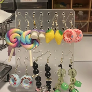 Färgglada örhängen med godis och frukt - Säljer ett gäng unika örhängen med coola motiv som klubbor i regnbågsfärger, donuts med strössel, citroner, svampar i olika färger, gröna kiwiskivor, svarta pärlor, rosa persikor och söta giraffer. Perfekt för dig som vill sticka ut med roliga och färgglada accessoarer.