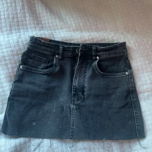 Svart jeanskjol från TRF - Säljer en svart jeanskjol från TRF med klassisk femficksdesign, rå kant nedtill och knapp- samt dragkedja framtill. Kjolen har en cool, lite tvättad look och är perfekt för dig som gillar streetstyle. Passar dig som vill ha en kort och edgy kjol. I storlek S💕