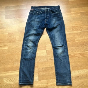 Blå jeans från Denim & Supply Ralph Lauren - Snygga blå jeans från Denim & Supply Ralph Lauren med klassisk femficksdesign och cool detalj med amerikansk flagga vid myntfickan. Jeansen har raka ben och är tillverkade i slitstarkt denimtyg. Perfekta för en avslappnad och trendig look. Obs, sömmen på vänstra bakfickan har börjat gå upp.