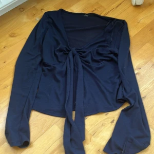 Marinblå långärmad omlottopp med knyt - Snygg svart omlottopp med långa ärmar och v-ringad hals. Framtill finns ett knyt som ger en cool detalj och lite draperad effekt. Tunn och mjuk, perfekt att styla med jeans eller kjol. Enkel men ändå trendig design som funkar till många looks.