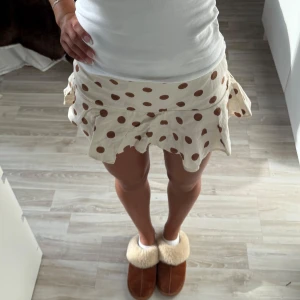 Prickig volangkjol i beige och brun - Superfin kort kjol med volangkant och bruna prickar på beige botten. Kjolen har en lätt utsvängd form och sitter snyggt i midjan. Från Zara i storlek xs!