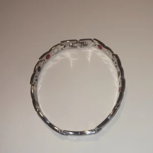 Silvrigt magnetarmband med detaljer - Snyggt magnetarmband i silverfärgad metall med länkar och twistade detaljer. Insidan har små runda färgade prickar i rött, svart och vitt som ger en cool och modern vibe. Perfekt för dig som gillar stilrena accessoarer med en twist.