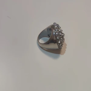 Glittrig silverring med stenar - Säljer en chunky silverfärgad ring med rund topp som är täckt av glittrande stenar. Ringen har en cool och iögonfallande design som verkligen sticker ut. Perfekt för dig som vill ha något extra till din outfit och gillar bling.