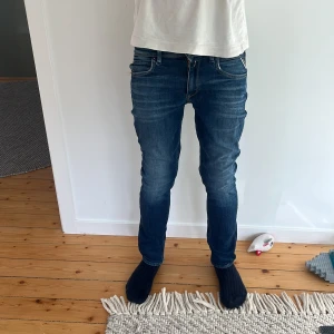Replay Anbass mörkblå jeans slim fit - Snygga Replay Anbass jeans i mörkblå tvätt med diskreta slitningar och klassiska fem fickor. Slim fit-modell med normal midja och raka ben. Jeansen är gjorda i stretchigt denim för skön passform och har Replay-logga på bakfickan.