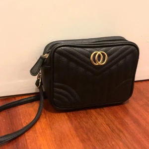 Svart axelväska från Primark - Snygg svart axelväska från Primark med quiltad design och gulddetaljer. Väskan har en praktisk dragkedja och justerbar axelrem. Perfekt för att bära dina nödvändigheter med stil.