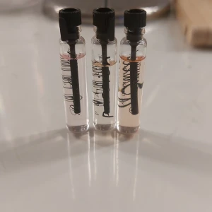 Tre parfymprover i glasflaskor - Säljer tre små parfymprover i genomskinliga glasflaskor med svarta lock. Varje flaska innehåller en ljusrosa vätska. Perfekt för att testa nya dofter innan du köper en större flaska.