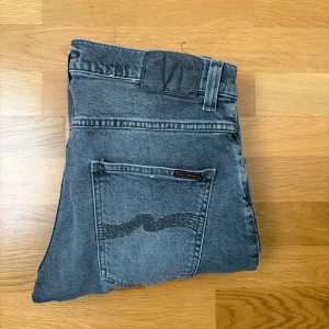 Grå jeans från Nudie Jeans - Snygga grå jeans från Nudie Jeans med en klassisk femficksdesign. De har en diskret tvättad look och en broderad detalj på bakfickorna. Perfekta för en avslappnad stil.