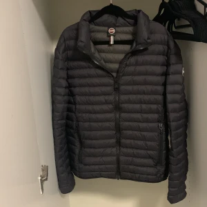 Svart pufferjacka från Colmar - Säljer en stilren svart pufferjacka från Colmar. Jackan har en dragkedja framtill och är långärmad. Perfekt för kyligare dagar med sin quiltade design. Märkeslogga syns på ärmen och insidan.