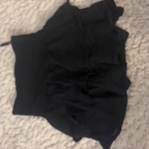 Svart kortkjol med volang - Snygg svart kortkjol med volangdetaljer. Perfekt för en trendig look. Kjolen har en tight passform och är gjord i ett mjukt material som ger en bekväm känsla.