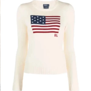 Vit stickad tröja med amerikansk flagga från Ralph Lauren - Säljer en vit stickad tröja från Ralph Lauren med en amerikansk flagga och RL-bokstäver på framsidan. Tröjan har långa ärmar och en ribbad nederkant. Perfekt för en stilren och klassisk look.