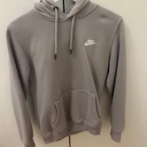 Grå hoodie från Nike - Säljer en stilren grå hoodie från Nike med klassisk logga på bröstet. Tröjan har en bekväm passform med långa ärmar. Nypris 800kr