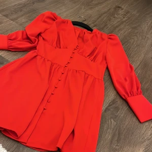 Röd klänning med knappar - Snygg röd klänning med långa ärmar och dekorativa knappar framtill. Perfekt för en färgstark look. Klänningen har en elegant passform och är gjord i ett mjukt material.