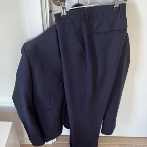 Mörkblå kostym Filippa K - Säljer en stilren mörkblå kostym med kavaj och byxor. Kavajen har en klassisk design med två knappar och fickor. Byxorna är raka och matchar kavajen perfekt. Perfekt för formella tillfällen. Fillipa K, exklusiv kostym