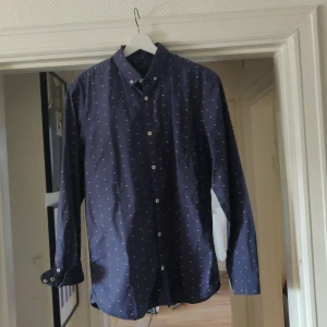 Mörkblå skjorta med små mönster - Snygg mörkblå skjorta från Selected Homme med små diskreta mönster. Skjortan har långa ärmar och knappar framtill. Perfekt för en stilren look.aldrig använd etiketten sitter fortfarande kvar, obs finns på fler sidor 