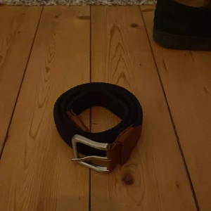 Svart och brunt bälte från Jack & Jones - Snyggt bälte från Jack & Jones i svart och brunt. Bältet har en klassisk design med en silverfärgad spänne och är tillverkat i en kombination av skinn och textil. Perfekt för att ge en stilren touch till din outfit.