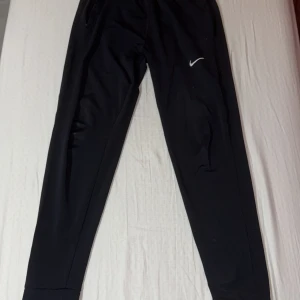 Svarta mjukisbyxor från Nike - Säljer ett par svarta mjukisbyxor från Nike med en liten vit logga på benet. Byxorna har en elastisk midja och är perfekta för en avslappnad stil. De är tillverkade i ett mjukt och bekvämt material. Är använda 2-3