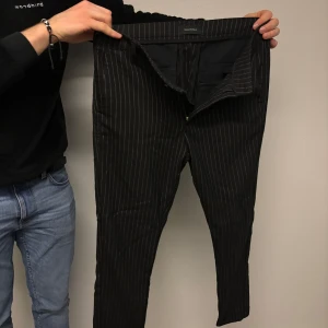 Svarta randiga byxor från Gabba - Snygga svarta byxor från Gabba med vita ränder. De har en dragkedja och är designade i Danmark. Perfekta för en stilren look.