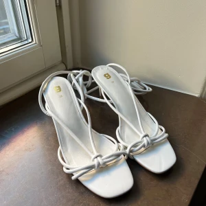 Vita sandaler med knytning - Snygga vita sandaler med elegant knytning och öppen tå. Perfekta för sommarens alla tillfällen. De har en stilren design med tunna remmar som ger en chic look.
